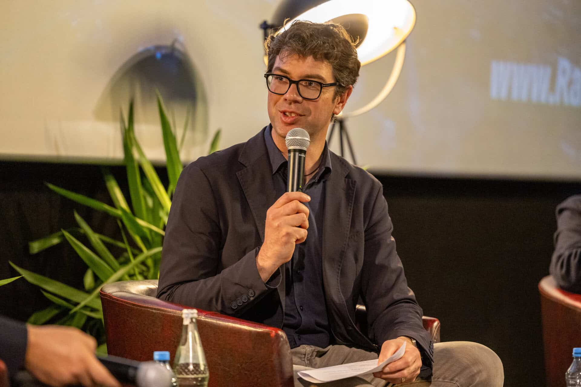 Ralf Nentwich, Mitglied des Landtags Baden-Württemberg, spricht bei einer Podiumsdiskussion und hält ein Mikrofon in der Hand
